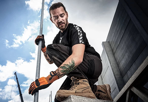 PUMA SAFETY CONQUEST HIGH Sicherheitsschuh S3 in Beige, getragen von einem Arbeiter mit Handschuhen auf einer Baustelle.