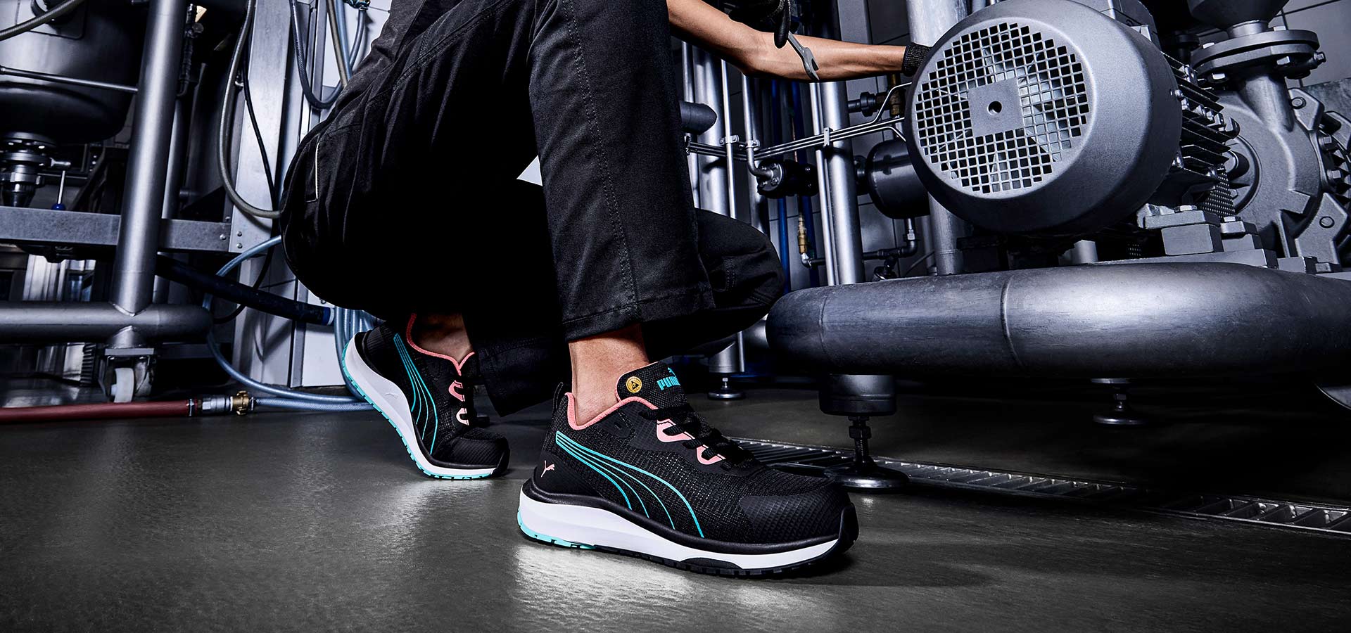 Schwarzer Puma Sicherheitsschuh CELERITY KNIT BLUE/CORAL LOW S1PS ESD FO HRO SR mit blauen Streifen und korallfarbenen Details, getragen bei Wartungsarbeiten in industrieller Umgebung.