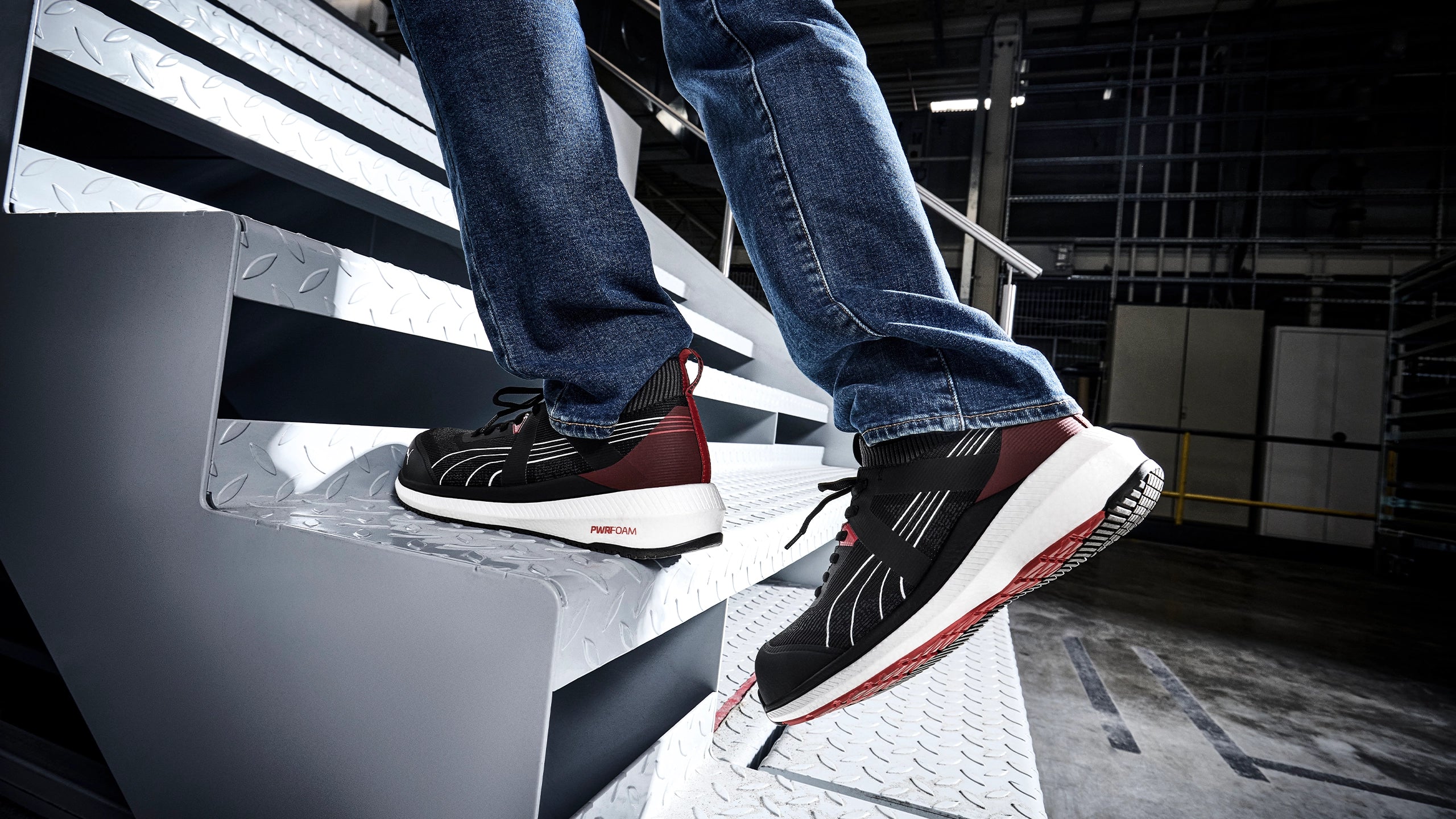 PUMA SAFETY TURBO LOW Sicherheitsschuh S1PS ESD in Schwarz mit roten Details, getragen von einer Person mit Jeans auf Metalltreppe.
