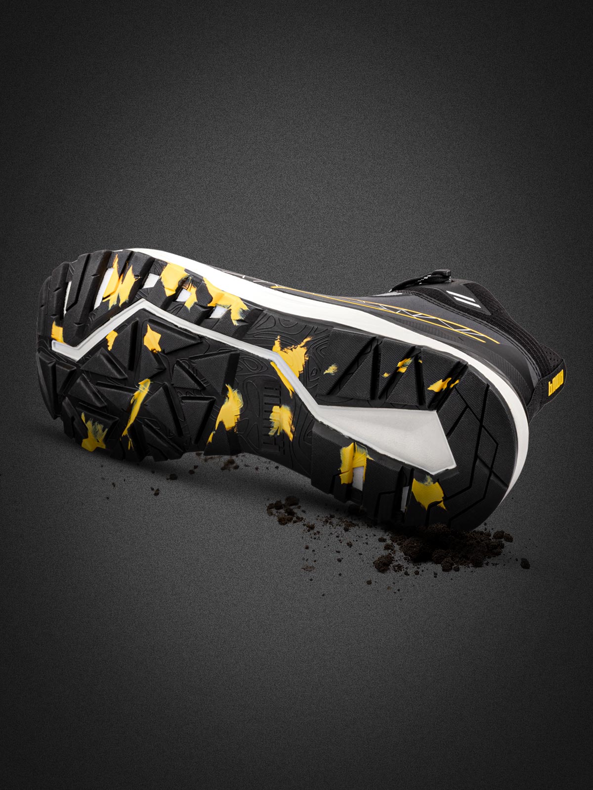 PUMA SAFETY XPLORE MID Sicherheitsschuh S3S ESD in Anthrazit mit gelben Akzenten, freigestellte Ansicht der profilierten Laufsohle mit gelben Markierungen und anhaftendem Schmutz vor dunklem Hintergrund